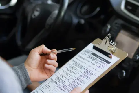 Persona revisa un formulario de solicitud de examen de manejo, preparándose para obtener su carnet coche automático.