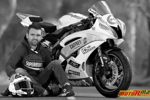 Czarno-białe zdjęcie motocyklisty Williama Dunlopa siedzącego obok swojego motocykla wyścigowego.