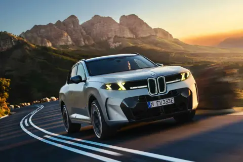 Nowe BMW X5 na krętej drodze wśród gór o zachodzie słońca.