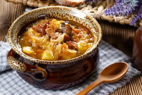 Gorący kapuśniak jak u babci, w glinianej misie, z kawałkami kiełbasy i ziemniaków, obok drewniana łyżka.
