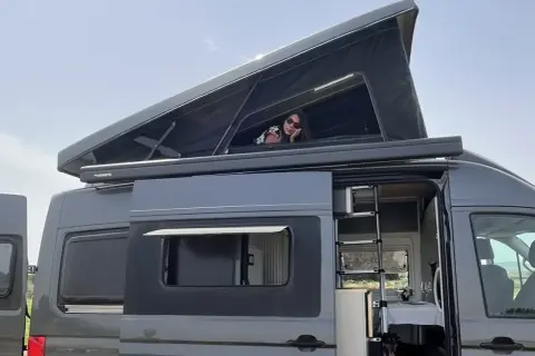 Mujer asomada en la cama elevada de una furgoneta camper. Las medidas de esta furgoneta man son perfectas para viajar.