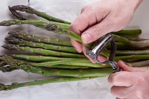 Mani che pelano asparagi verdi con un pelapatate. Impara come pulire gli asparagi per una preparazione perfetta.
