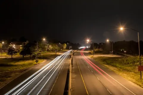 Luces de coches dejan estelas blancas y rojas en la carretera de noche, iluminada por el alumbrado de carretera.