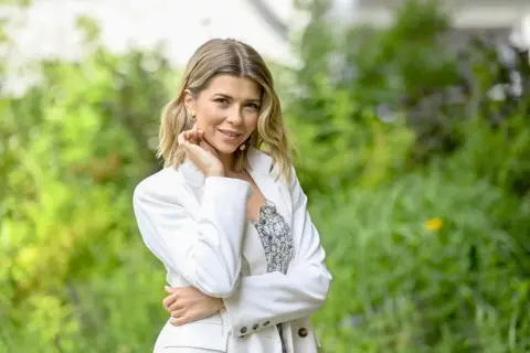 Agnieszka Dziekan z Koła Fortuny, uśmiechnięta, w białej marynarce, na tle zieleni.