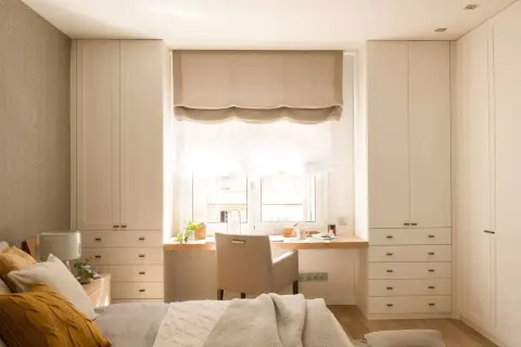 Escritorio funcional para aprovechar espacio bajo ventana, con armarios a ambos lados.