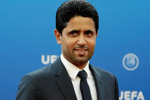 Nasser Al-Khelaifi, właściciel PSG, w eleganckim garniturze na tle niebieskiej ściany z logo UEFA.