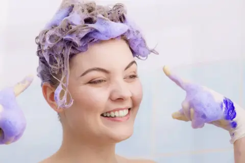 Sonrisa radiante con cabello teñido de violeta, lista para el antes y después. Guantes con espuma violeta.