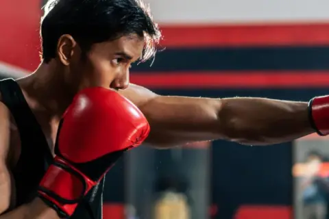 Boxer throws a powerful punch, aiming for the sternum. Red gloves flash as he trains in the ring.