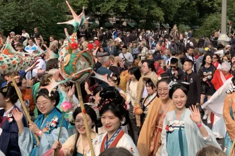 Bunte Drachenköpfe und Menschen in traditionellen Gewändern beleben den **Carnival Berlin**. Eine fröhliche Parade zieht durch die Menge.