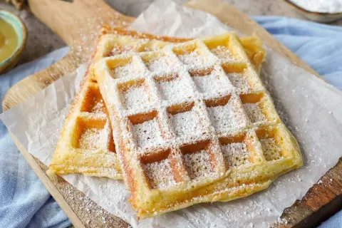 Zwei fluffige Waffeln, bestäubt mit Puderzucker, auf einem Holzbrett. Ein perfektes Rezept für fluffige Waffeln!