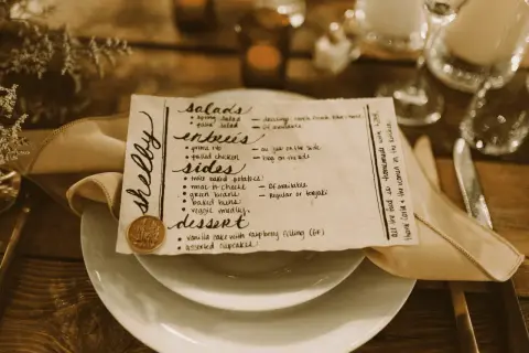Un menu de mariage manuscrit, joliment présenté sur une assiette, détaille les entrées, accompagnements et desserts.