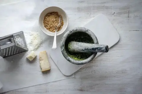Mortel med grön pesto, riven parmesan, nötter och rivjärn. Ingredienser för ett klassiskt pesto recept.