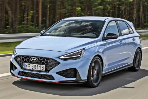 Błękitny Hyundai i30 N, sportowy hatchback, pędzi po drodze wśród drzew.