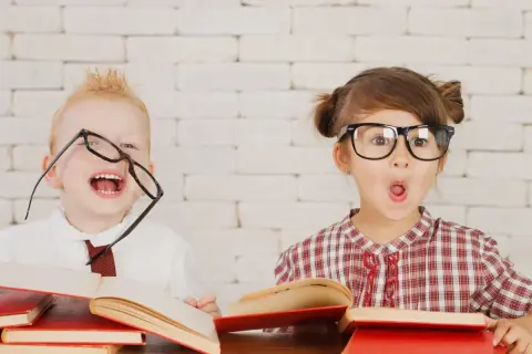 Dzieci z okularami i książkami, wesołe i zaskoczone. Wczesna pedagogika w praktyce, rozbudzająca ciekawość świata.