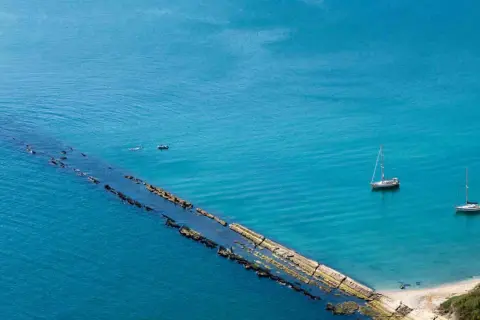 La spiaggia del Trave, con le sue acque turchesi, ospita due barche a vela e un piccolo motoscafo.
