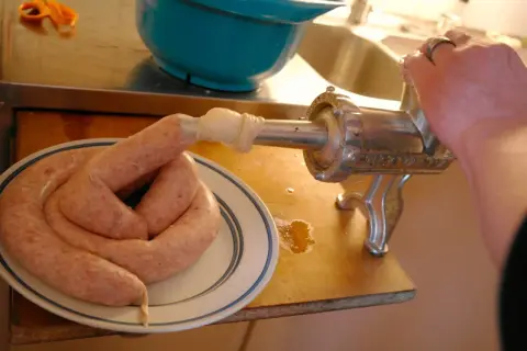 En hand vrider på en köttkvarn som gör korv. Ett korv-recept blir verklighet på tallriken.