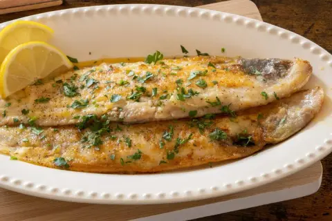 Delicioso lenguado a la plancha, dorado y jugoso, adornado con perejil fresco y rodajas de limón.