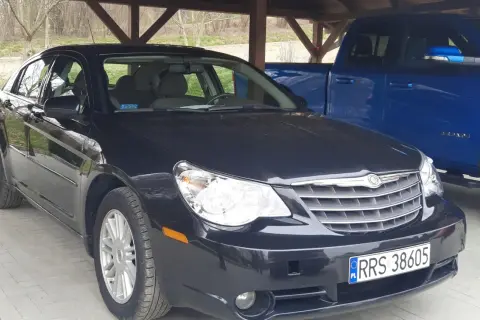 Czarny Chrysler Sebring pod wiatą, obok niebieski pickup.