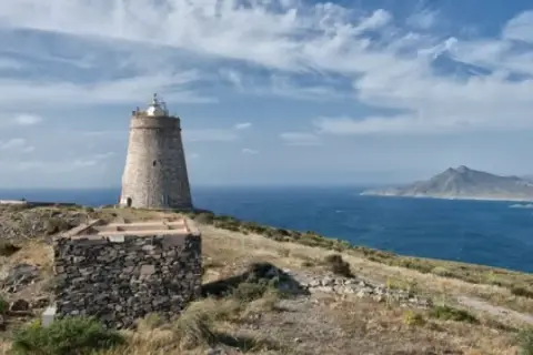 El faro de Almería se alza sobre una colina rocosa, vigilando el mar azul bajo un cielo nublado.