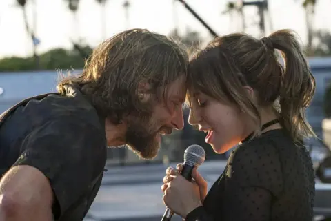 Bradley Cooper i Lady Gaga śpiewają razem, zbliżając twarze do mikrofonu.