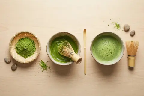 Préparation du matcha : poudre verte dans un panier, pâte dans un bol avec un fouet, et boisson mousseuse dans un autre bol. Le tout sur fond de bois clair.