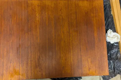 Förbereder för att slipa teak. En träyta ligger på svart plast, bredvid en slipmaskin och en trasa.