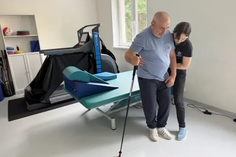 Rehabilitacja po udarze niedokrwiennym. Pacjent z pomocą fizjoterapeuty ćwiczy chód z laską. Rokowania są dobre.
