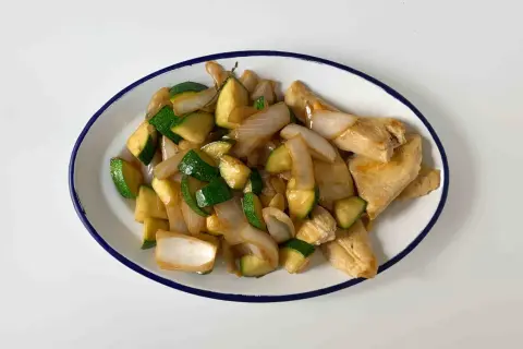 Sabroso pollo con calabacín y cebolla salteados, servido en un plato blanco con borde azul.
