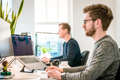 Deux développeurs travaillent sur leurs ordinateurs portables, plongés dans le code. Une scène typique d'une école de développeur moderne.
