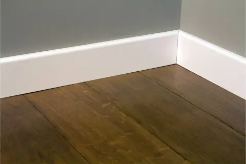 Esquina de una habitación con suelo de madera oscura y rodapiés blancos lisos, mostrando diferentes tipos de rodapiés.