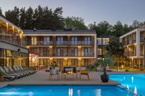 Nowoczesny hotel z basenem i leżakami, otoczony drzewami.