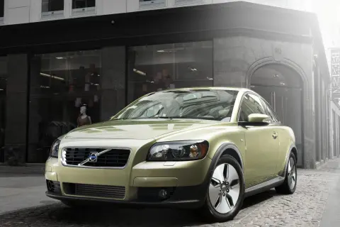 Złoty Volvo C30 segment c zaparkowany na brukowanej ulicy przed sklepem z modą.