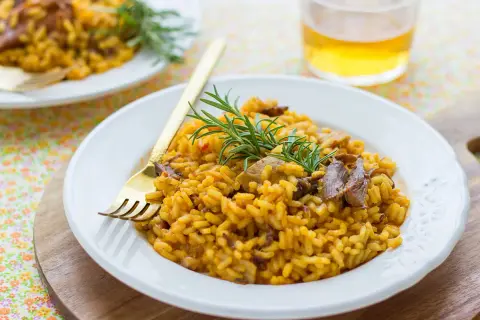 Delicioso arroz con secreto ibérico y setas, adornado con romero fresco. Un plato principal perfecto.