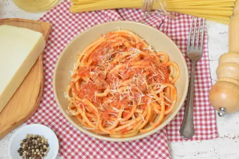 Pyszne bucatini amatriciana z pomidorowym sosem i parmezanem, obok kawałek sera i pieprz.