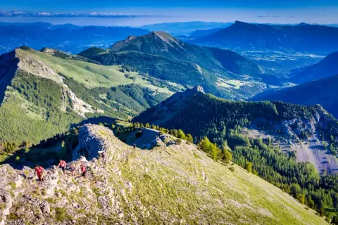 Randonneurs sur la crête rocheuse menant au pic de Gleize, avec des montagnes verdoyantes et un ciel bleu.