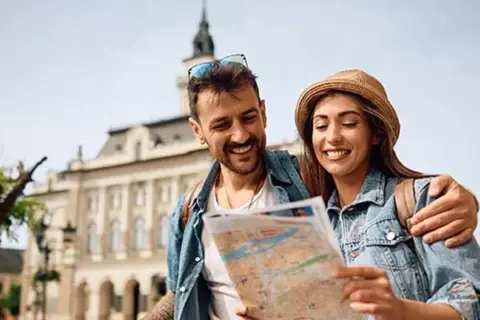 Uśmiechnięta para planuje wyjazd na weekend, studiując mapę na tle zabytkowej architektury.