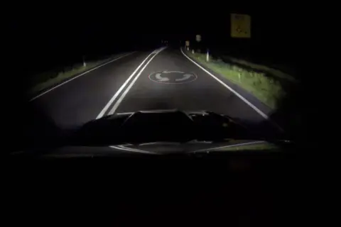 La route de nuit, éclairée par les feux de route, révèle un rond-point.
