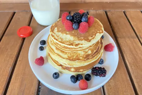 Pancake light con frutti di bosco e un bicchiere di latte su un tavolo di legno.
