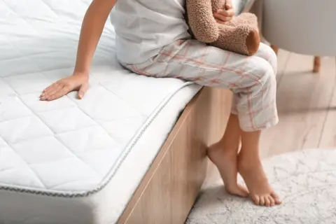 A child sits on a new mattress, wondering how long does a hybrid mattress take to expand.