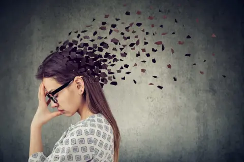 Kobieta z ręką na czole, której głowa rozpada się na fragmenty. Obraz symbolizuje **adhd z przewagą zaburzeń koncentracji uwagi**, trudności w skupieniu myśli.