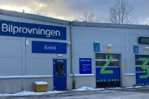 Bilprovningen med entré och garageportar för besiktning. En varningstriangel syns inte, men bilen är redo för kontroll.