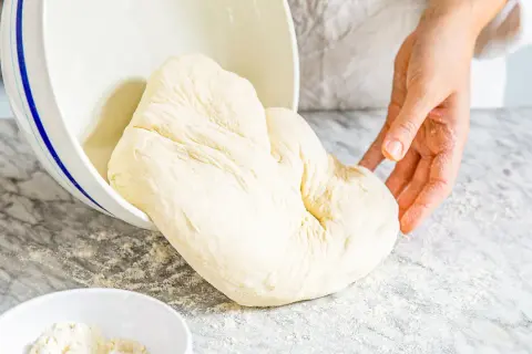 Frischer Pizzateig wird aus einer Schüssel auf eine bemehlte Arbeitsfläche gegeben. Das Mehl ist der Schlüssel für den perfekten Pizzaboden.