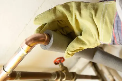Hand mit Handschuh isoliert Kupferrohre, um Heizungsrohre zu verlegen und Energieverlust zu minimieren.