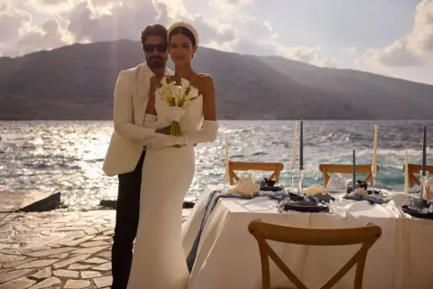 Un couple marié, maridat 19 63, pose près de la mer. La mariée tient un bouquet de callas. Une table de réception est dressée.