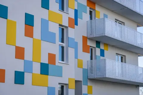 Nowoczesny budynek z kolorowymi, geometrycznymi panelami i białymi balkonami.