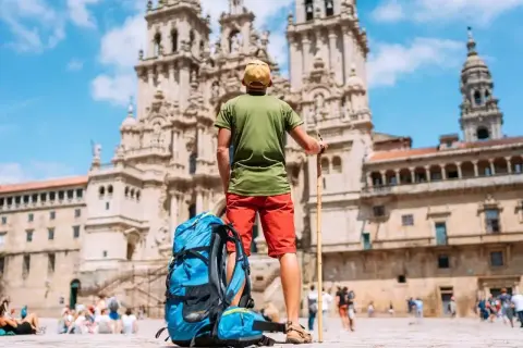 Pielgrzym z plecakiem i laską przed katedrą w Santiago de Compostela. Święta w El Camino to cel podróży.