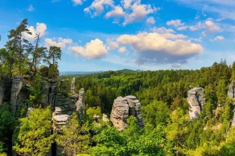 Felsformationen und grüne Wälder laden zum tschechien wandern ein. Ein malerischer Ausblick unter blauem Himmel mit Wolken.