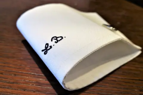 Un dettaglio di una camicia bianca piegata, con le iniziali "F.B." ricamate in nero.