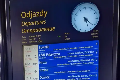 Tablica odjazdów pociągów z informacją o opóźnieniach, wskazująca na utrudnienia w ruchu pociągów. Zegar pokazuje aktualny czas.