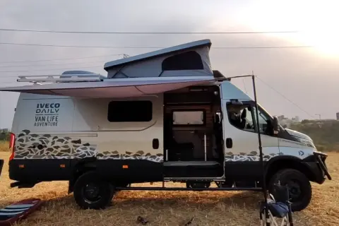 Ce **modèle camion** Iveco Daily aménagé pour le "Van Life Adventure" est prêt pour l'exploration, avec son toit relevable et son auvent déployé.
